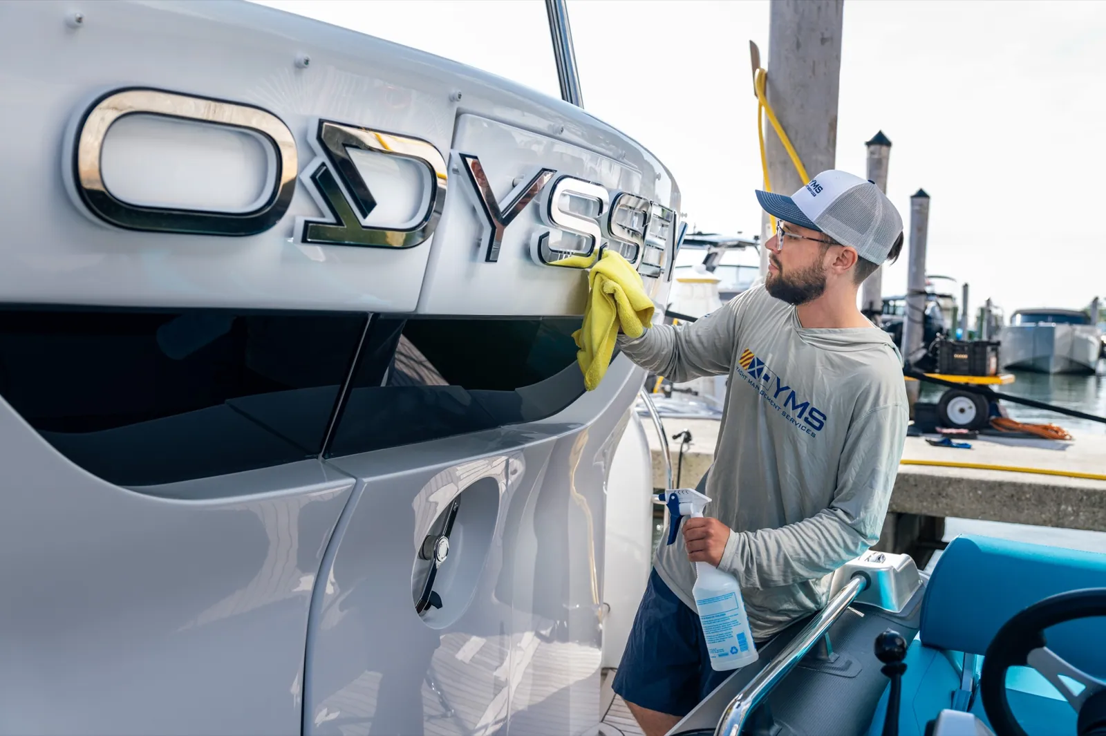 A YMS crew member washing the transom of a yacht with the name ODYSSEA on the hull