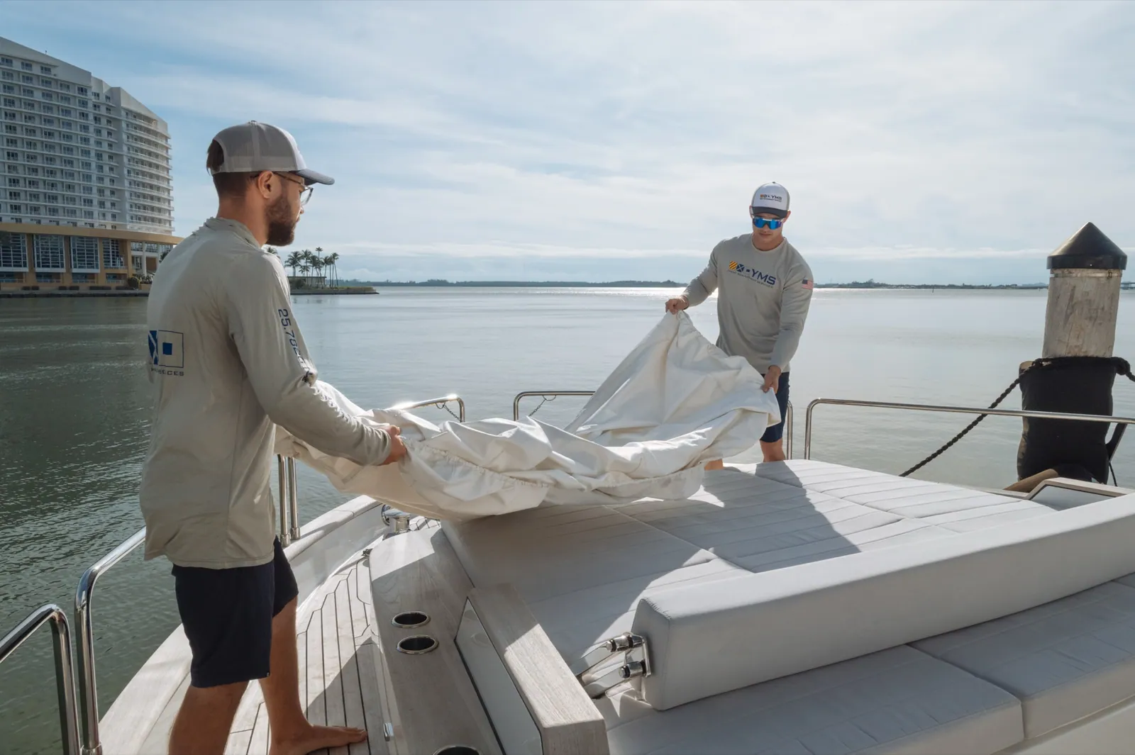 Two YMS crew stretching a white cover over an aft deck, flat open water behind