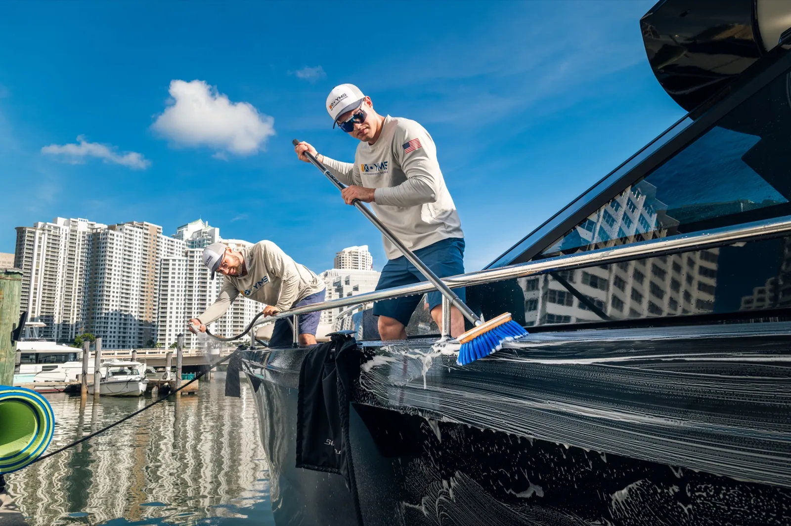 A YMS crew member leaning over the rail to brush the hull, blue sky and skyline behind
