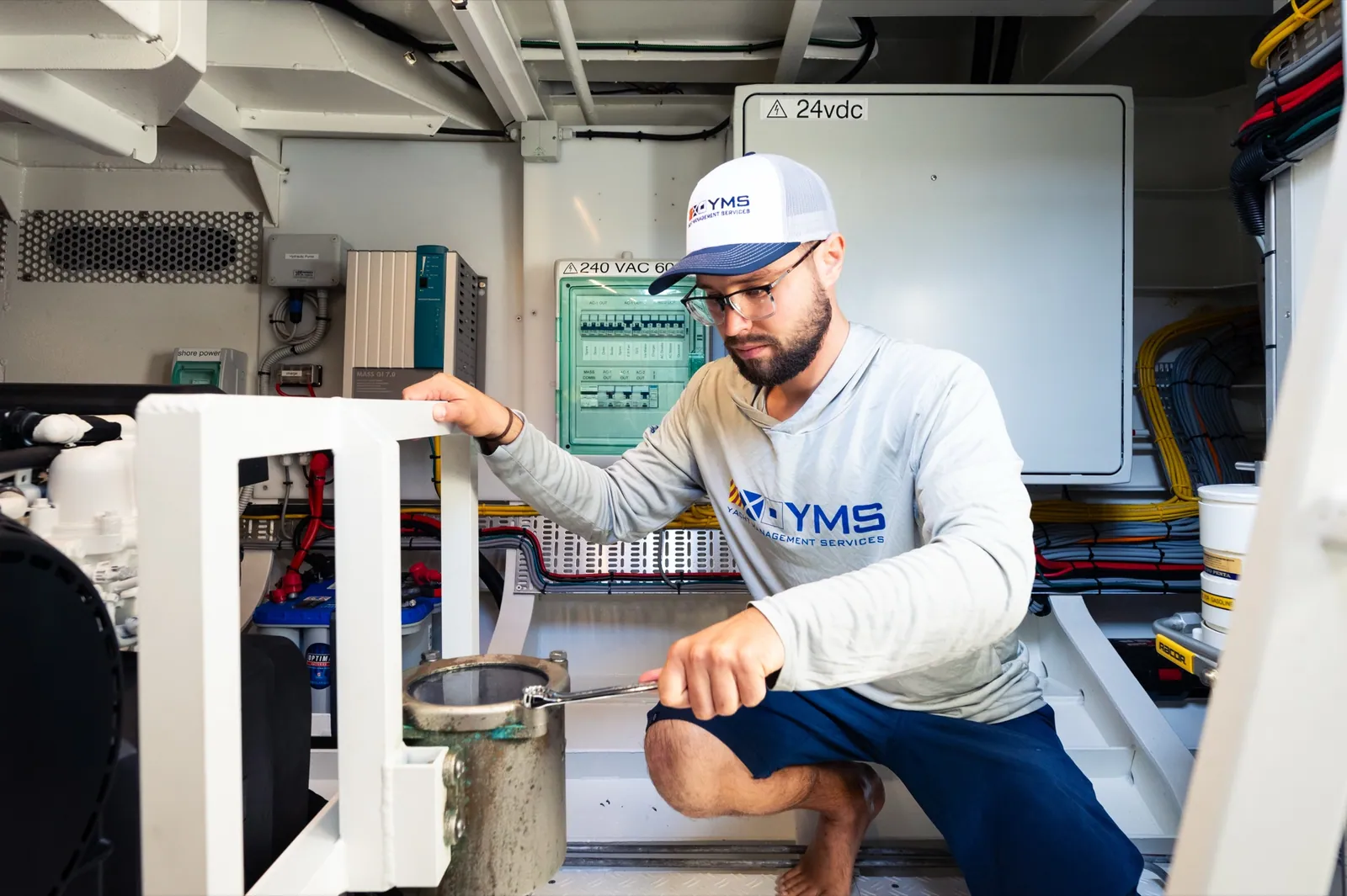 A YMS technician kneeling at a systems panel in a bright yacht interior