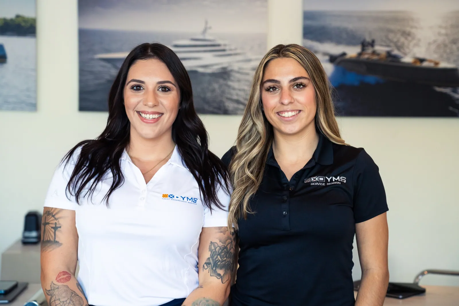 Two YMS team members in branded polos in the Fort Lauderdale office, fleet photography on the wall behind them