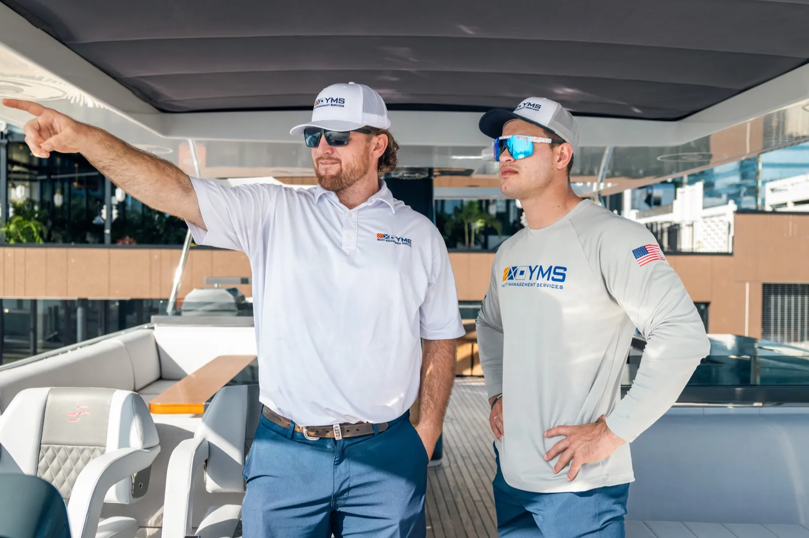 Two YMS crew standing in a yacht cockpit under the hardtop, one pointing off frame